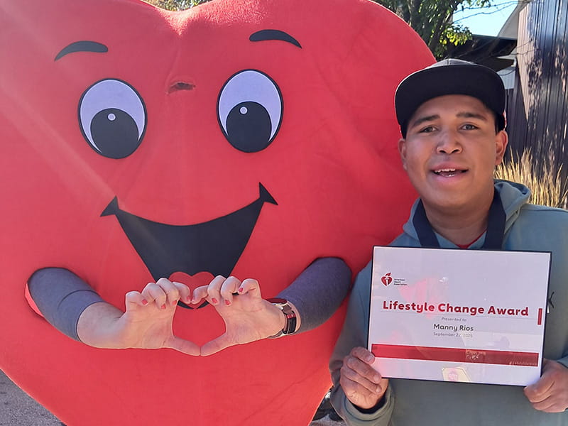 Manny Rios with the Lifestyle Change Award standing next to an American Heart Association heart mascot at the Milwaukee 2025 Heart Walk