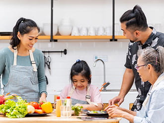 a family with parents, a young daughter, and a grandmother are gathered in the kitchen making a meal together