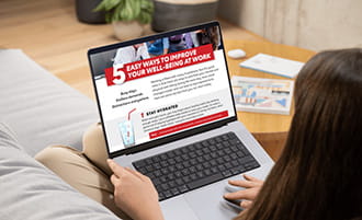 View over a woman's shoulder of her laptop screen displaying "5 Easy Ways to Improve Your Well-Being at Work Infographic"