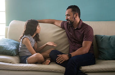 dad sitting on couch talking with young daughter