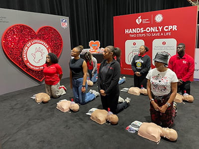 A group of AHA Scholars on their knees lined up with CPR manikins flanked by American Heart Association CPR signage