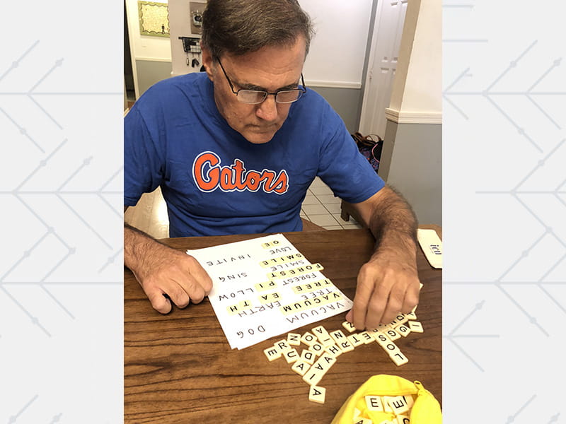 Carlos Lopez practicing home rehab using a word game with letter tiles scattered on the table