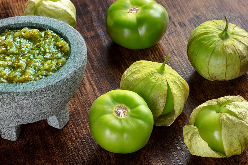 tomatillos frescos en una mesa junto a un plato de salsa de tomatillo
