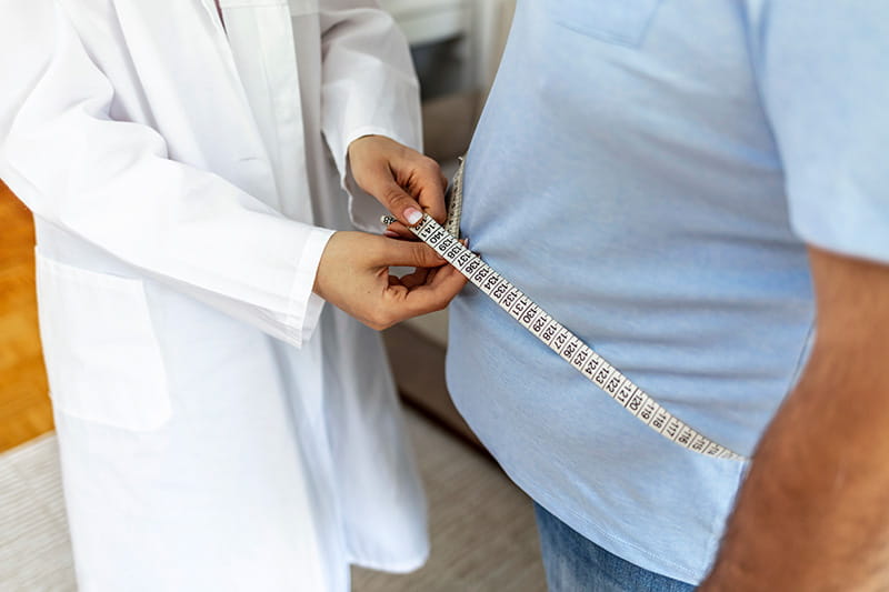 focus on a man's waist as a healthcare professional measures it with a tape measure