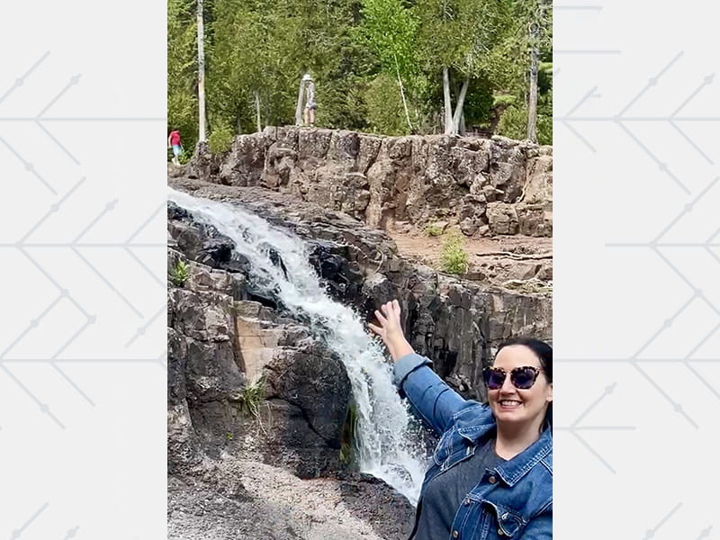 Jackie Newgent gesturing towards a waterfall on a hike in Beaver Bay, Minnesota