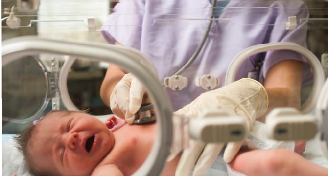 Newborn baby in an incubator being examined by nurse