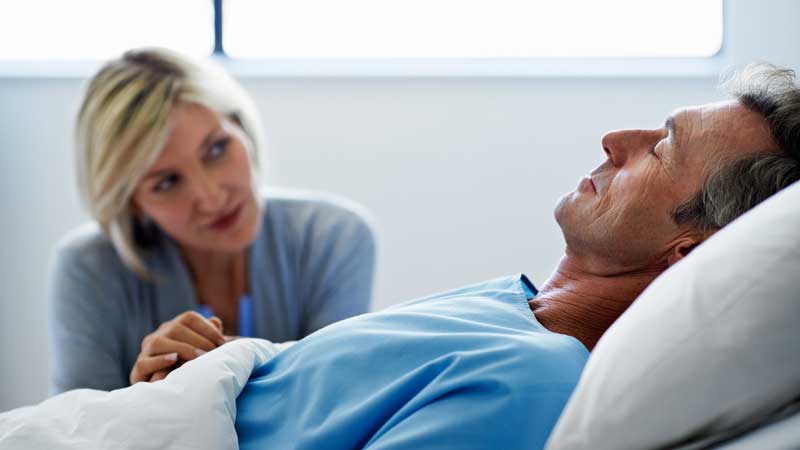 esposa sentada junto al esposo en la cama del hospital