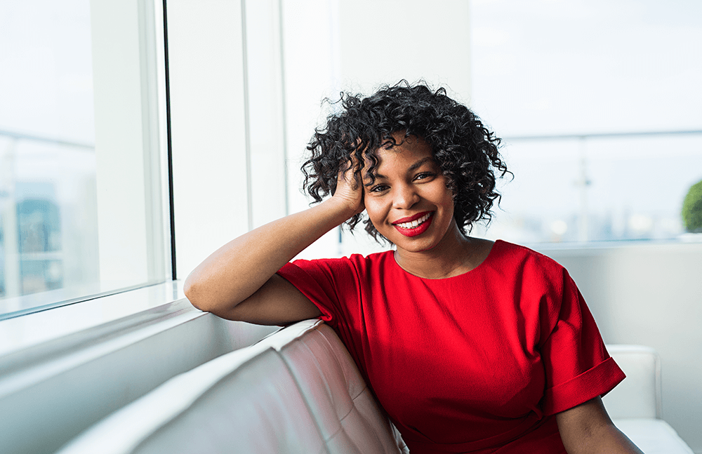 woman in red dress sitting on a sofa by the window