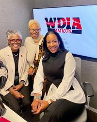 Dr. Rubye Taylor Drake,  Bev Johnson and Kyna Shine are posing together and smiling with a TV screen showing WDIA in the background.