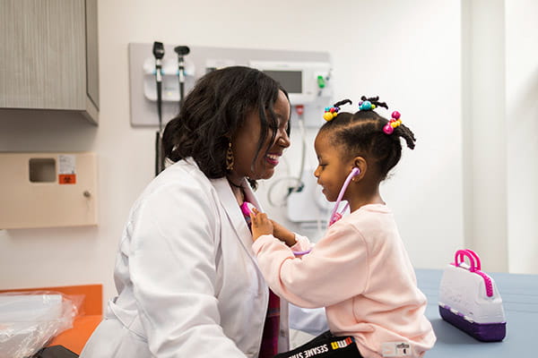 A young Black girl is using a stethoscope to listen to the heartbeat of her Black female doctor in a patient room. A young Black girl is using a stethoscope to listen to the heartbeat of her Black female doctor in a patient room.